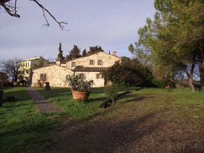 A stone building with a paved path leading to it, surrounded by greenery and trees. - Albergo Il Colombaio (Castellina in Chianti)