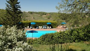A pool area with lounge chairs and umbrellas, surrounded by greenery and trees. - Albergo Il Colombaio (Castellina in Chianti)