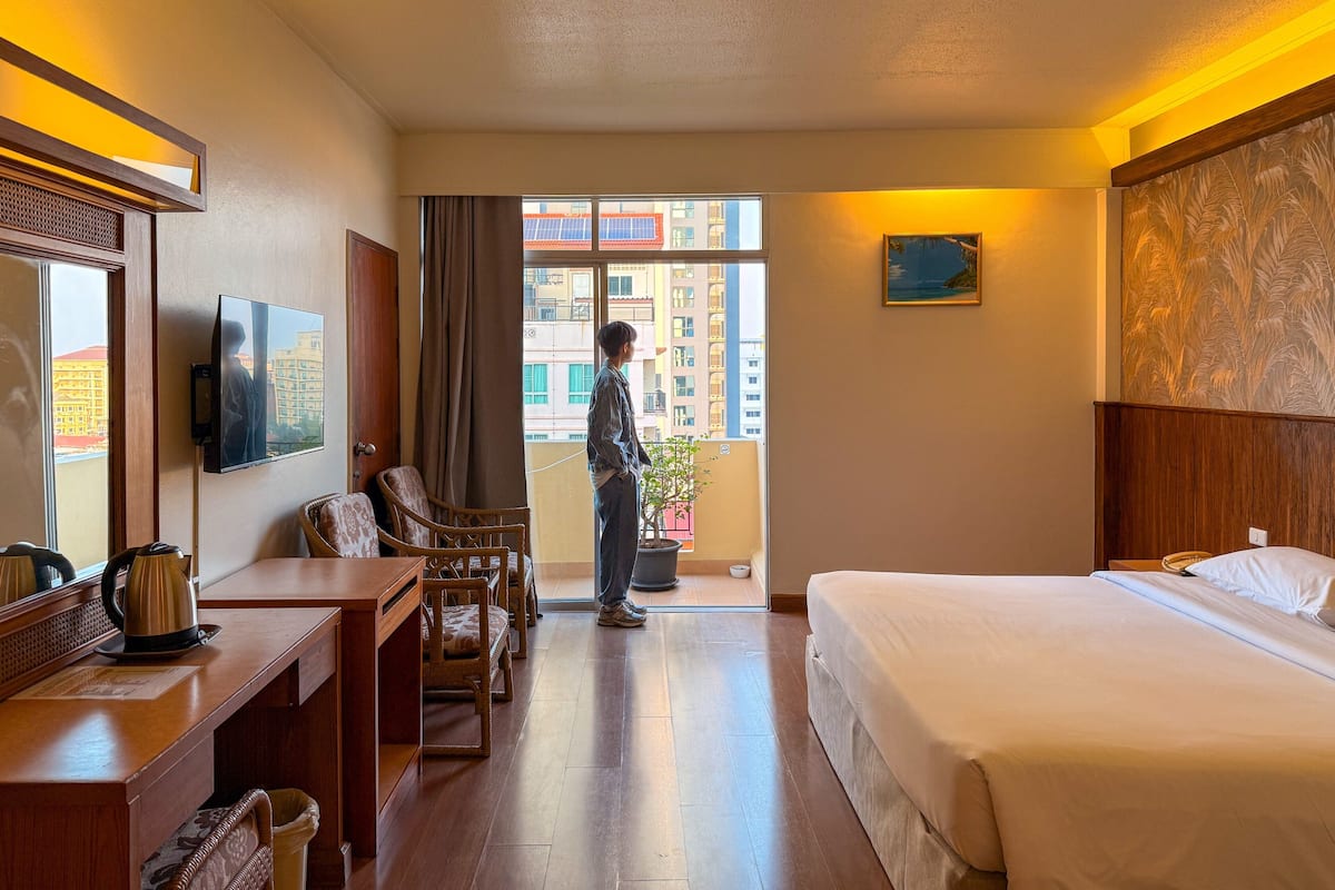 Une chambre d’hôtel comprenant un lit, un bureau avec une bouilloire, une chaise, une télévision et un balcon offrant une vue sur les bâtiments.