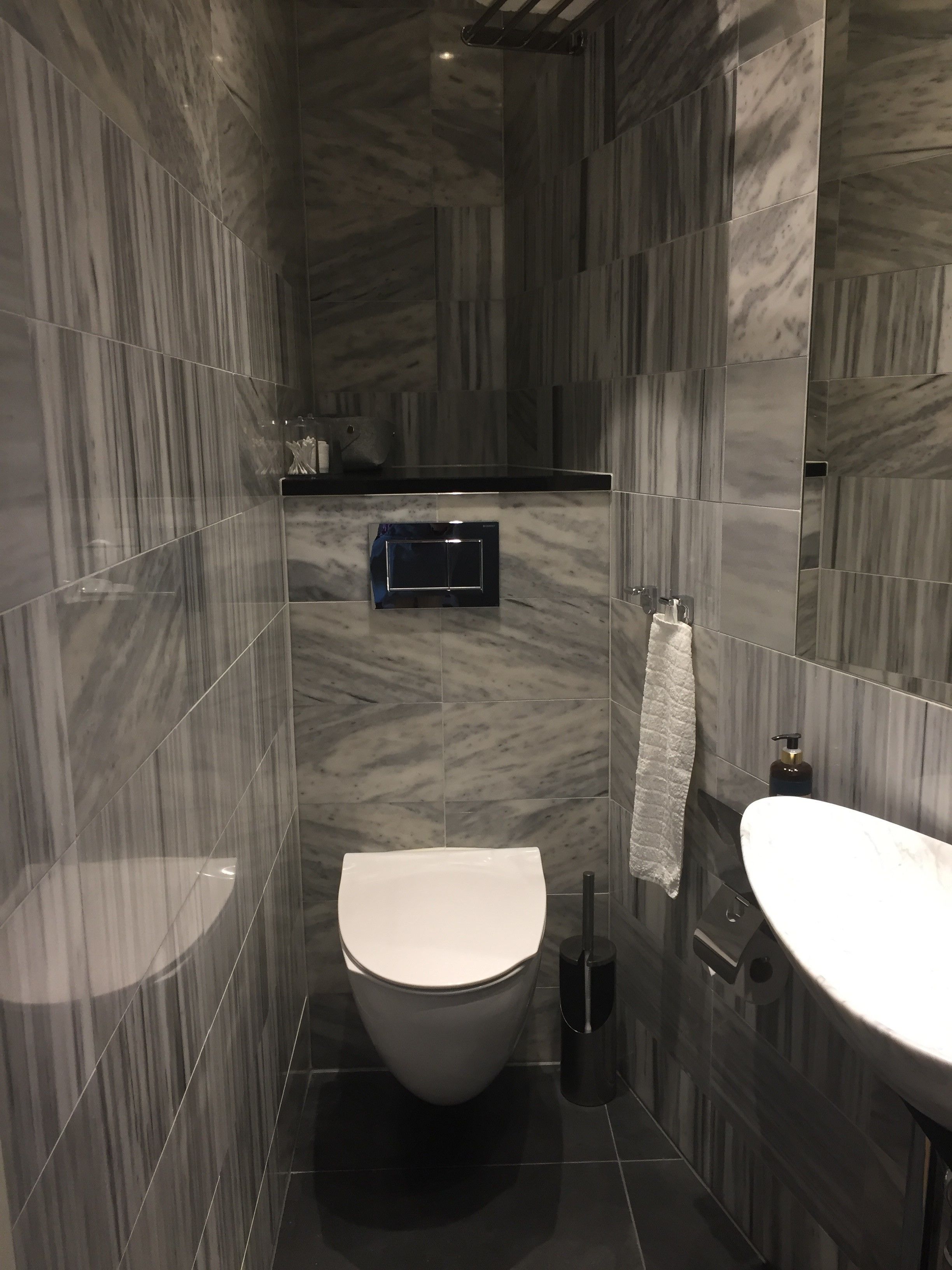 Un baño moderno con diseño de pared de mármol, un inodoro, un lavabo y una toalla colgada en la pared.