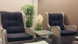 Een set rieten meubels met gewatteerde stoelen en een tafeltje, een groene kussen en een plant in pot.