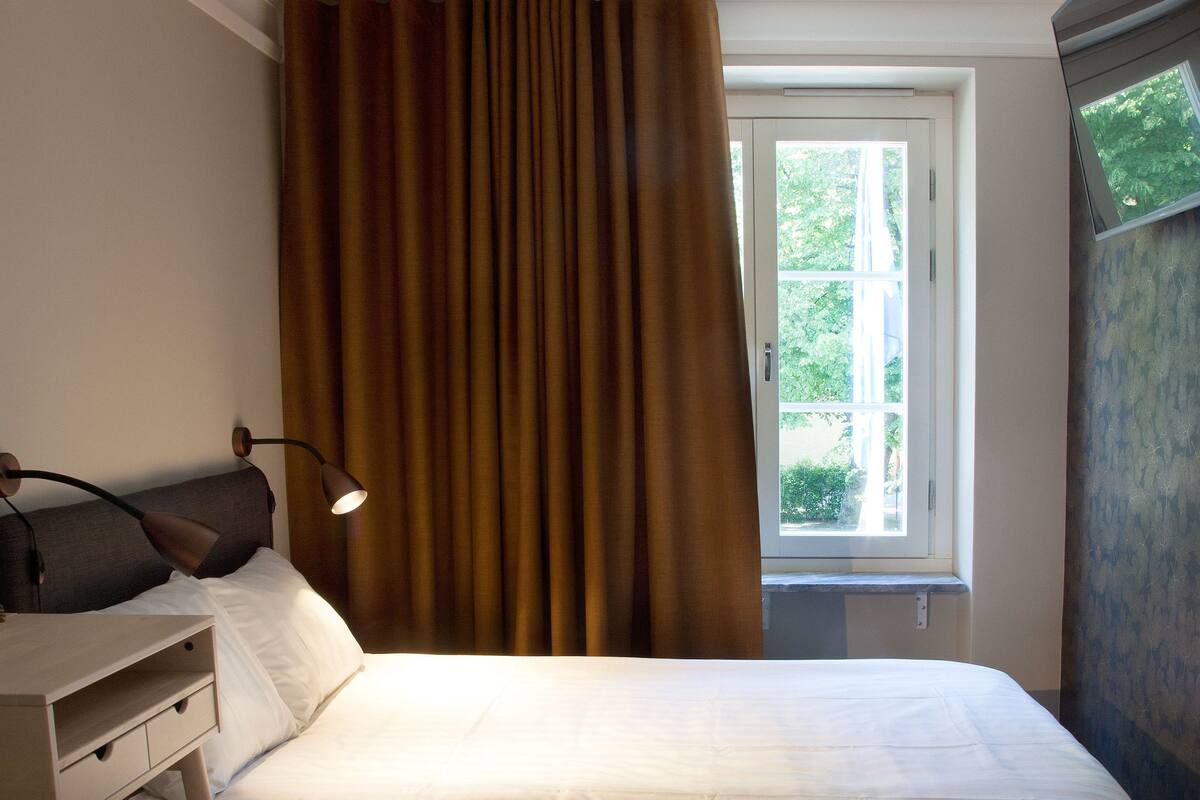 A bedroom with a bed, a desk, a lamp, and a window with curtains.