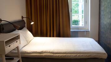 A bedroom with a bed, a desk, a lamp, and a window with curtains.