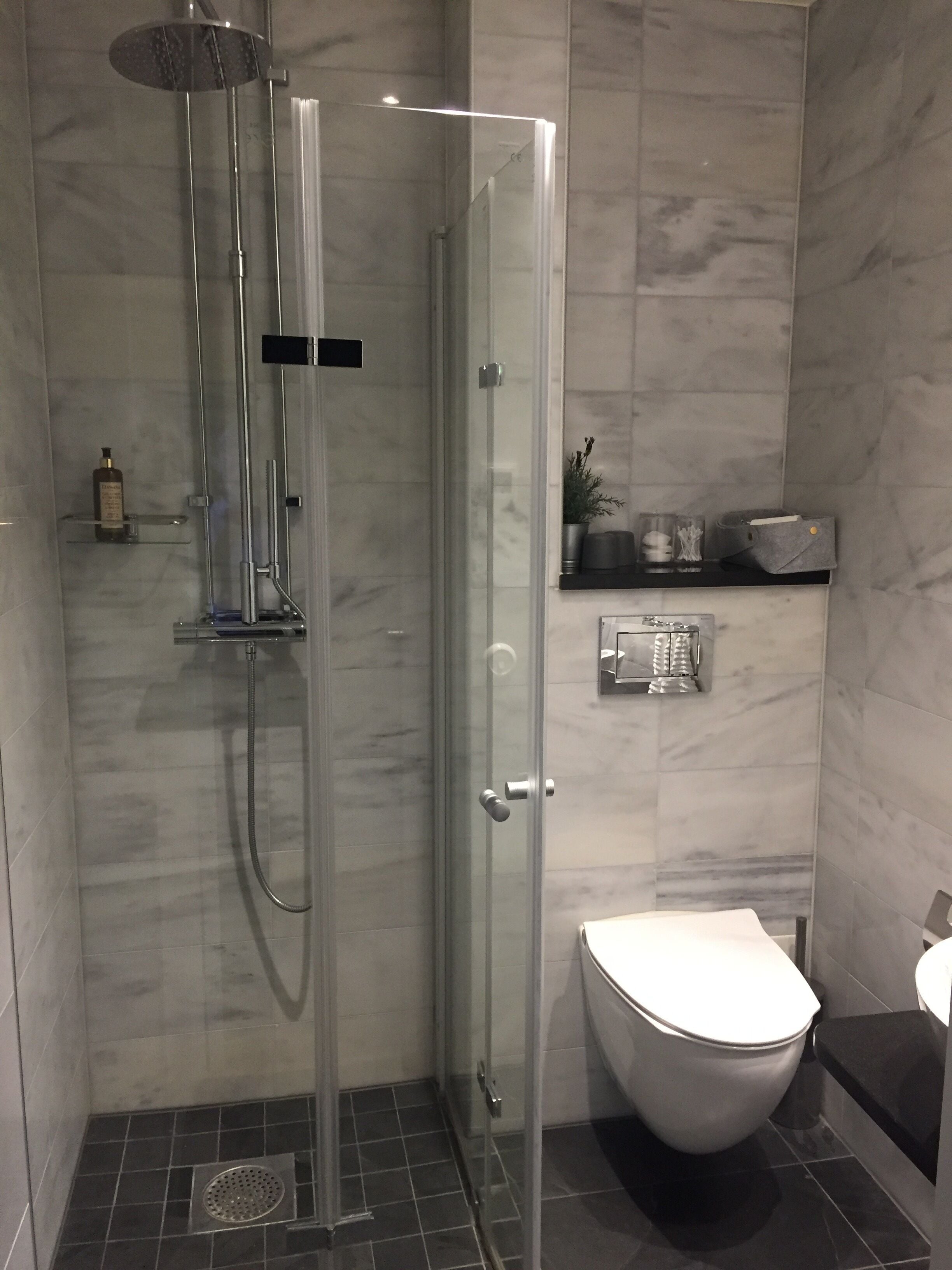 Un baño moderno con ducha acristalada, inodoro y estante con artículos de aseo.