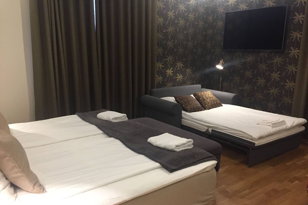A hotel room with two beds, a flat-screen TV mounted on the wall, and a wooden floor.