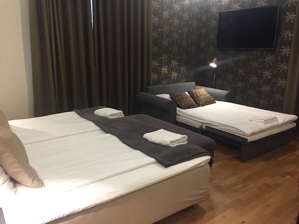 A hotel room with two beds, a flat-screen TV mounted on the wall, and a wooden floor. - Södra Hotellet (Norrköping)