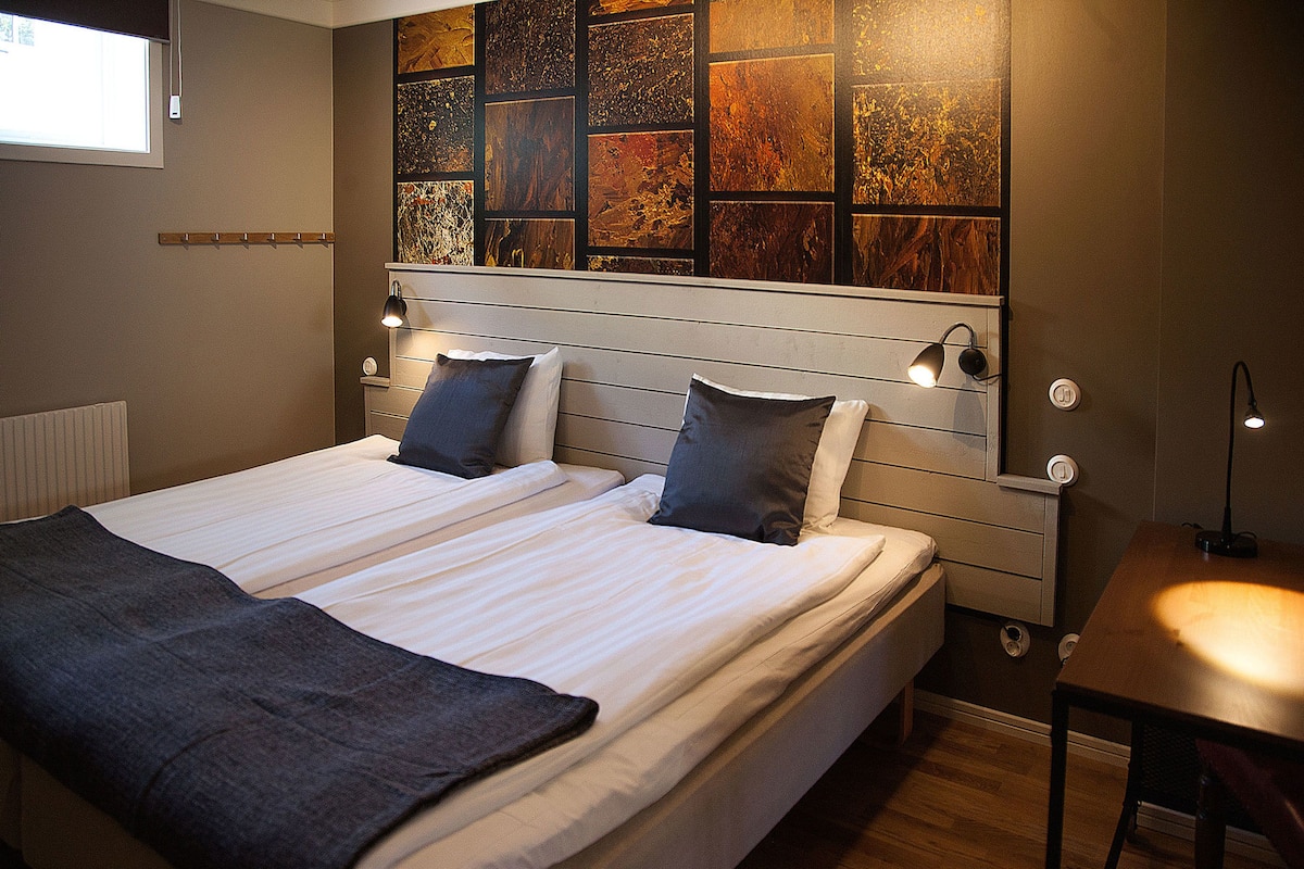 A double bed with two pillows, a bedside table, and a wall with a wooden panel design.