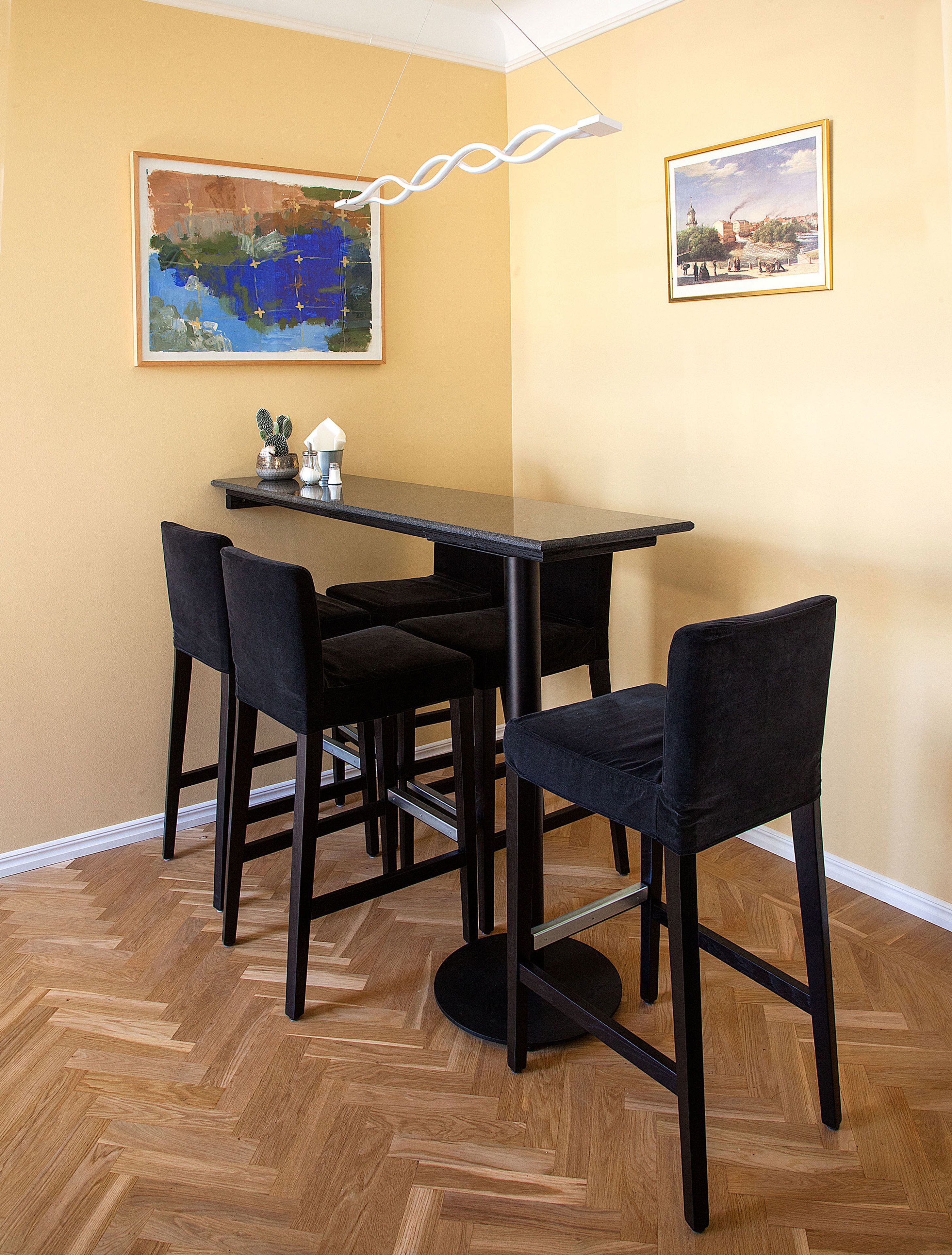 A dining area with a table and four chairs, two framed paintings on the wall, and a cactus on the table.