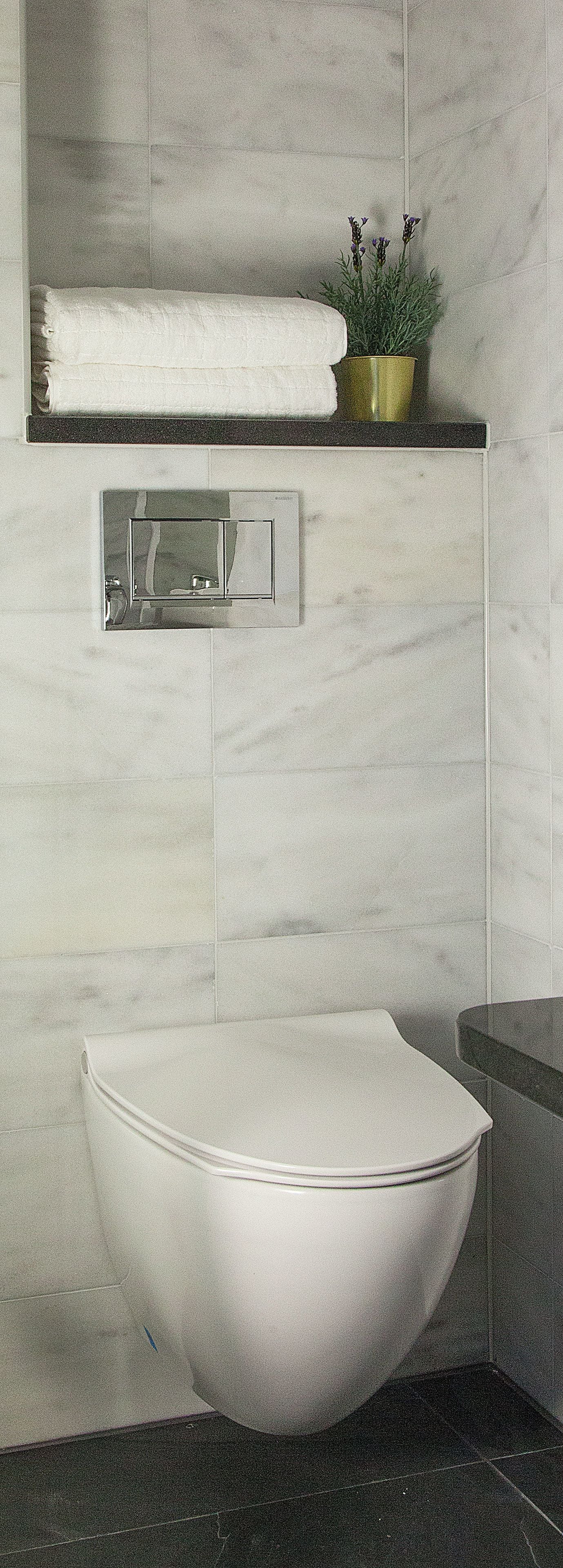 A modern bathroom with a white vessel sink, a towel rack with folded towels, and a small potted plant on a black countertop.