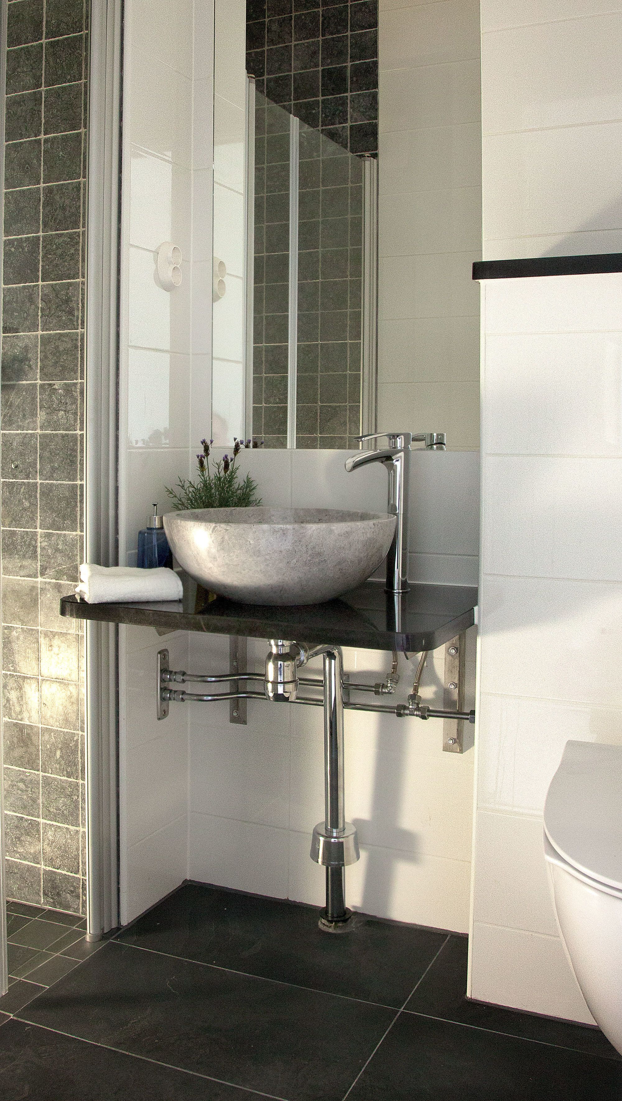 A modern bathroom with a large, round, stone sink, chrome fixtures, and a tiled floor.
