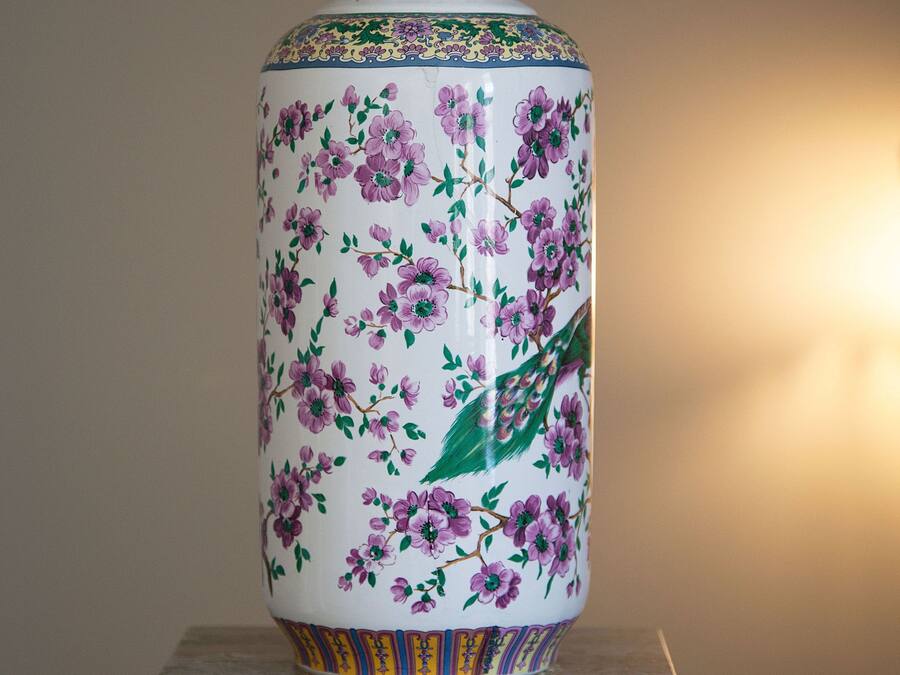 Um vaso grande com motivos florais sobre um pedestal.