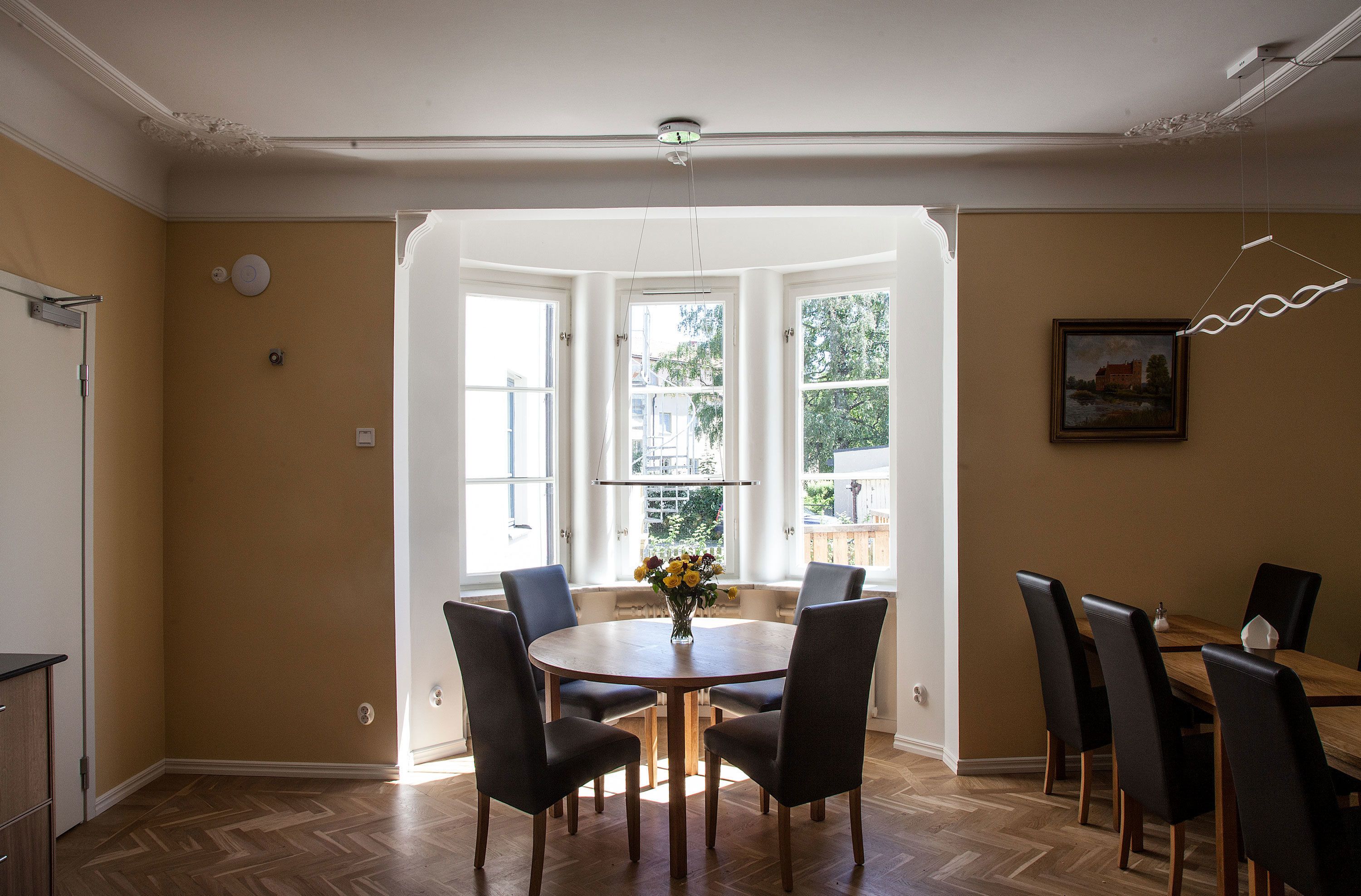 Un comedor con una mesa redonda de madera, sillas negras y un jarrón de flores.