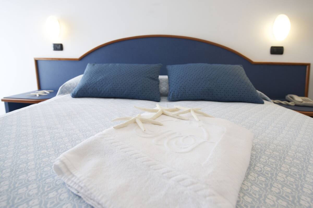A neatly made bed with a blue headboard, two pillows, and a white towel with a floral design.