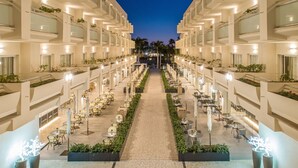 A hotel atrium with a central walkway flanked by dining areas and balconies, featuring modern architecture and indoor plants. - Hotel Maspalomas Princess-All Inclusive (San Bartolomé de Tirajana)