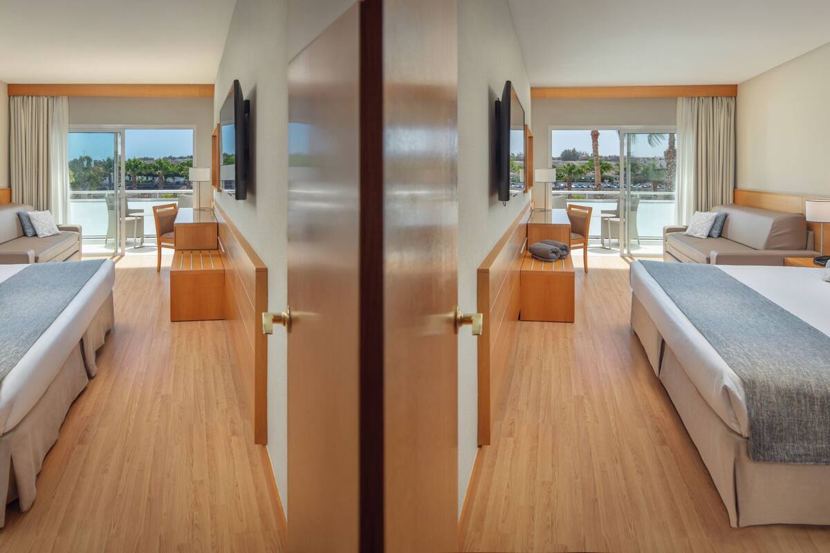 A hotel room with two beds, a sofa, a desk, and a balcony with a view.