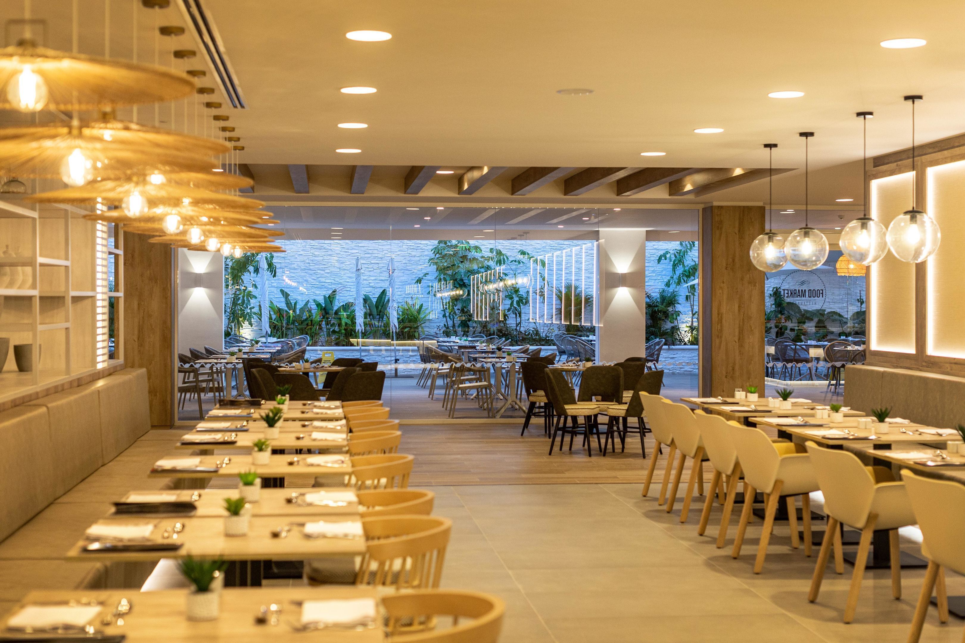 A restaurant with multiple tables and chairs, a view of the outdoor area, and a stone wall.