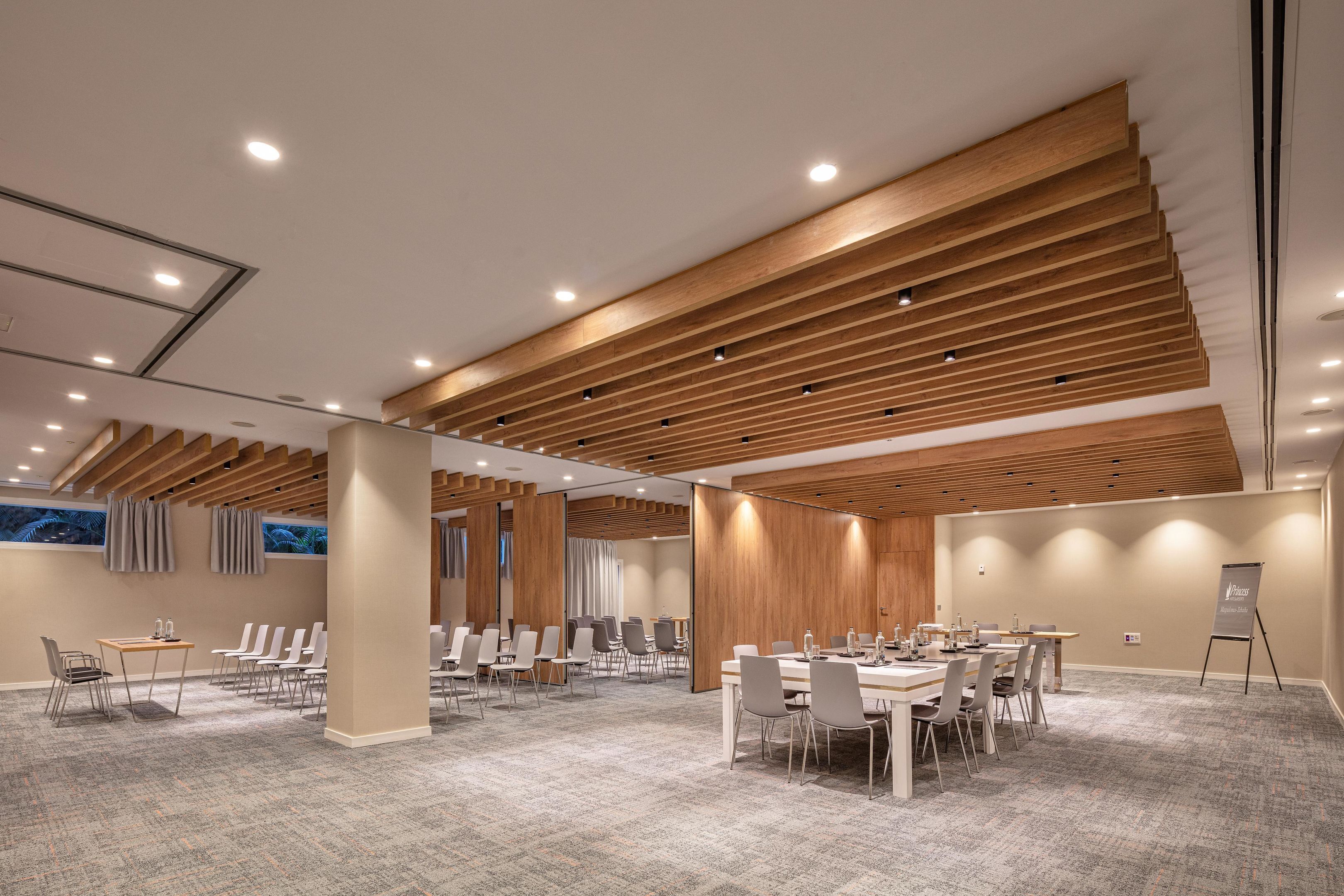 A modern conference room with wooden ceiling beams, carpeted floors, and a large table with chairs.