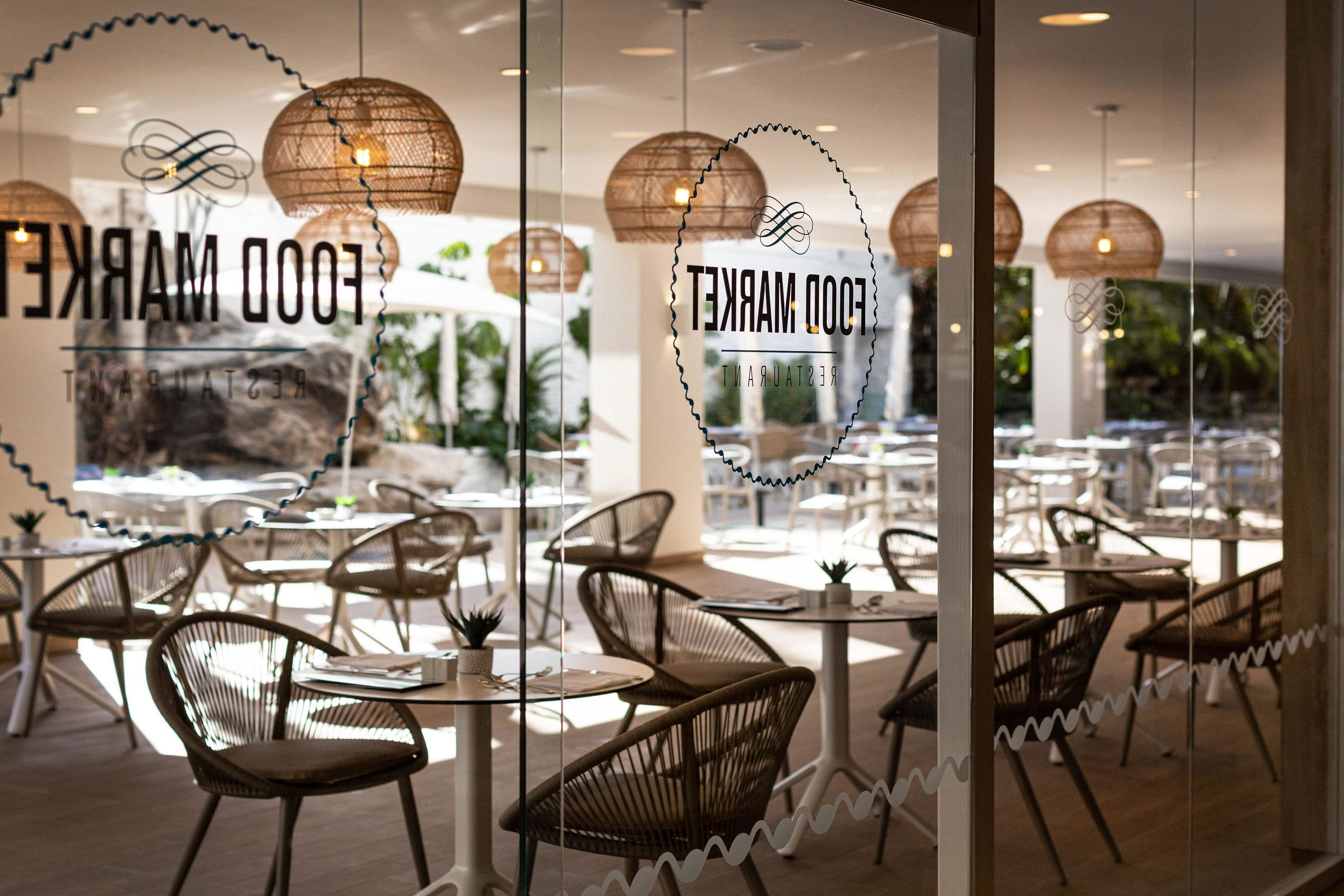 Un restaurante con sillas y mesas de mimbre, y vistas del exterior a través de amplios ventanales.