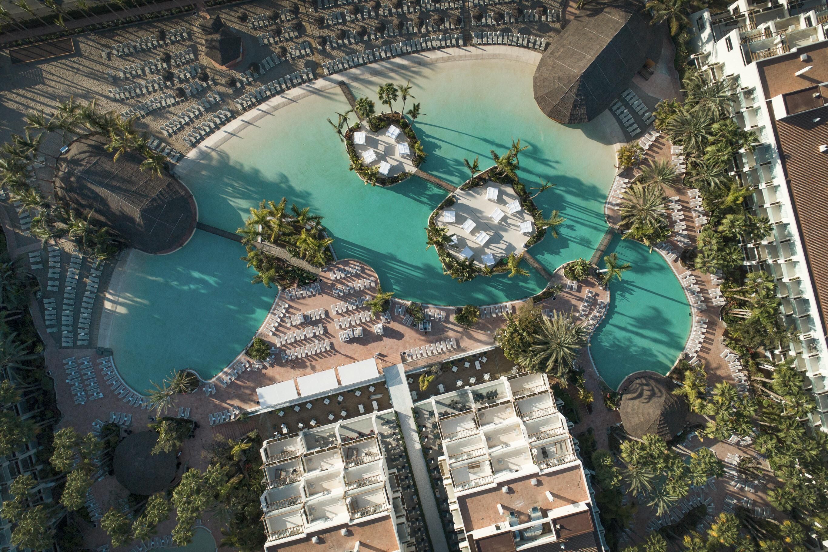 An aerial view of a resort with a large central pool, multiple lounge areas, and a variety of accommodations.