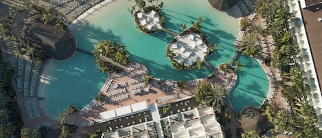 An aerial view of a resort with a large central pool, multiple lounge areas, and a variety of accommodations.