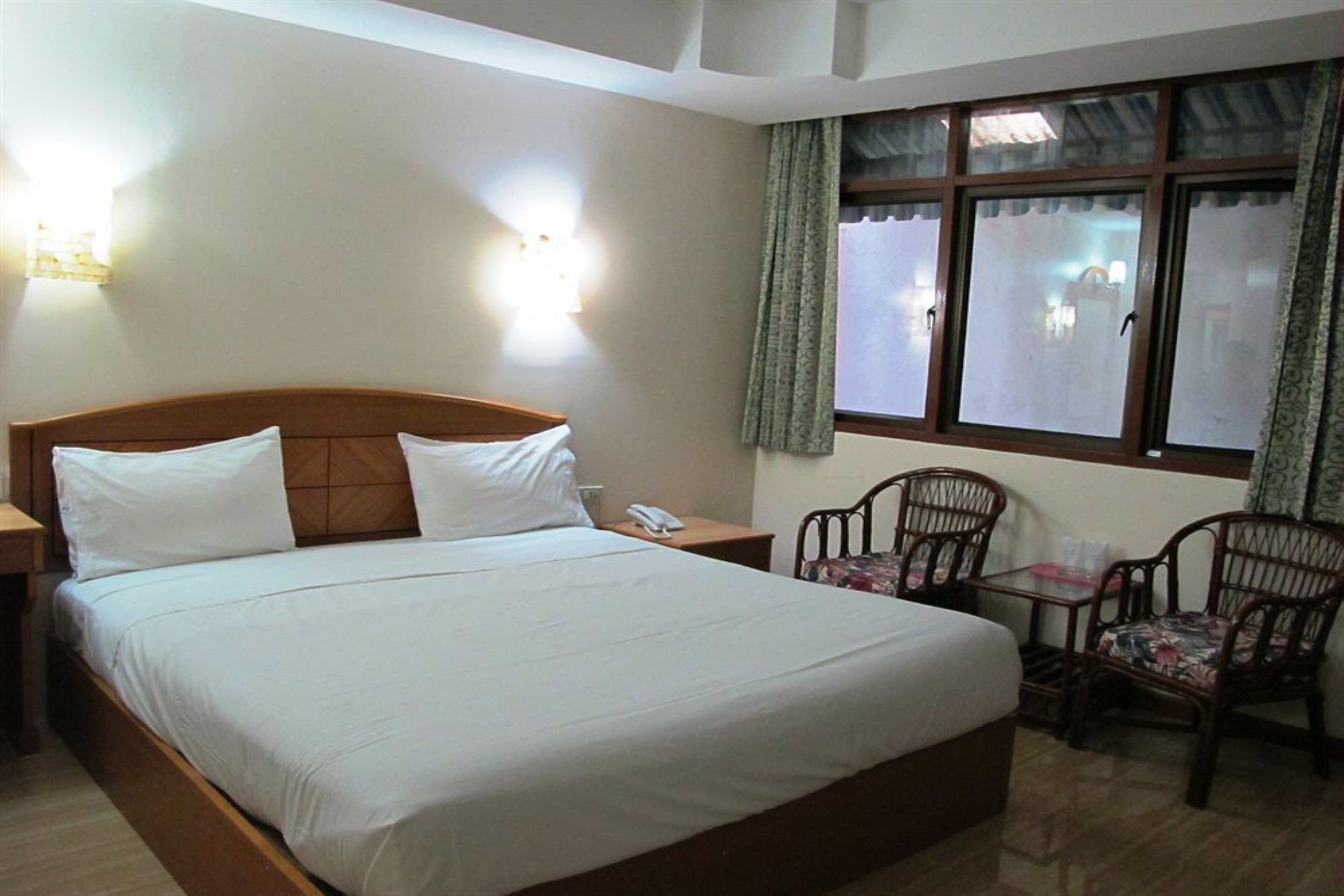 Une chambre d’hôtel avec un grand lit, deux tables de chevet, une petite table avec des chaises et une fenêtre avec des rideaux.