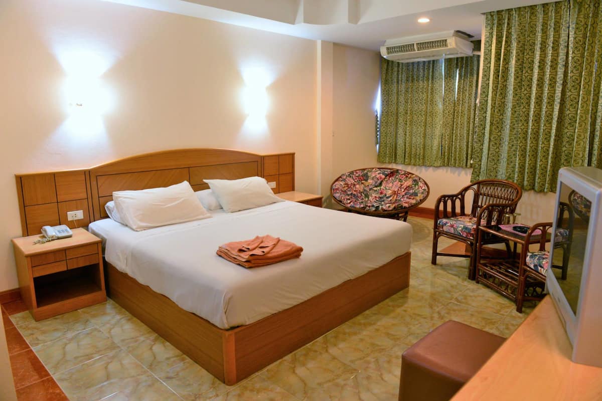 A hotel room with a wooden bed, a nightstand, a chair, and a television.