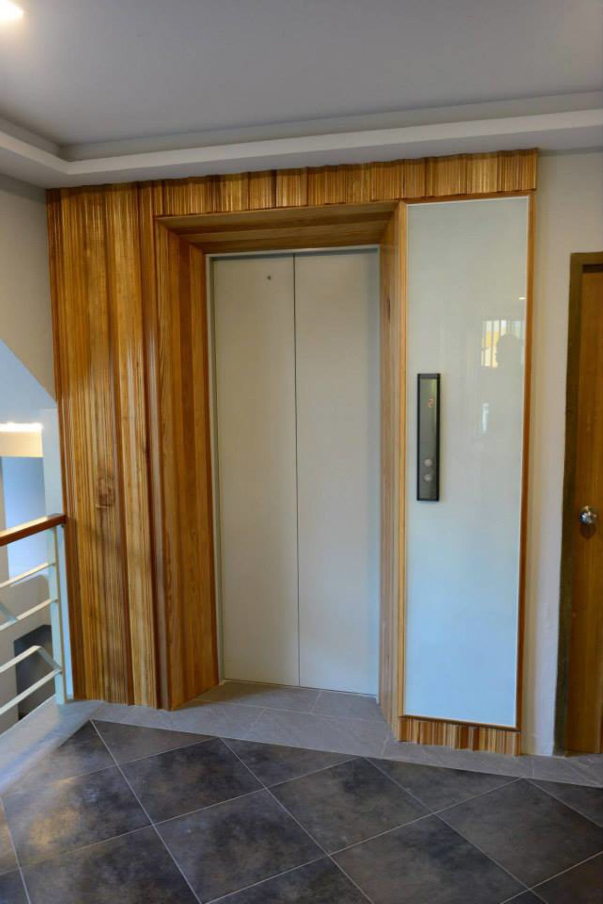 A hallway with a wooden panel wall, a white door with a keypad, and a tiled floor.
