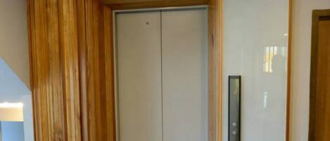 A hallway with a wooden panel wall, a white door with a keypad, and a tiled floor.