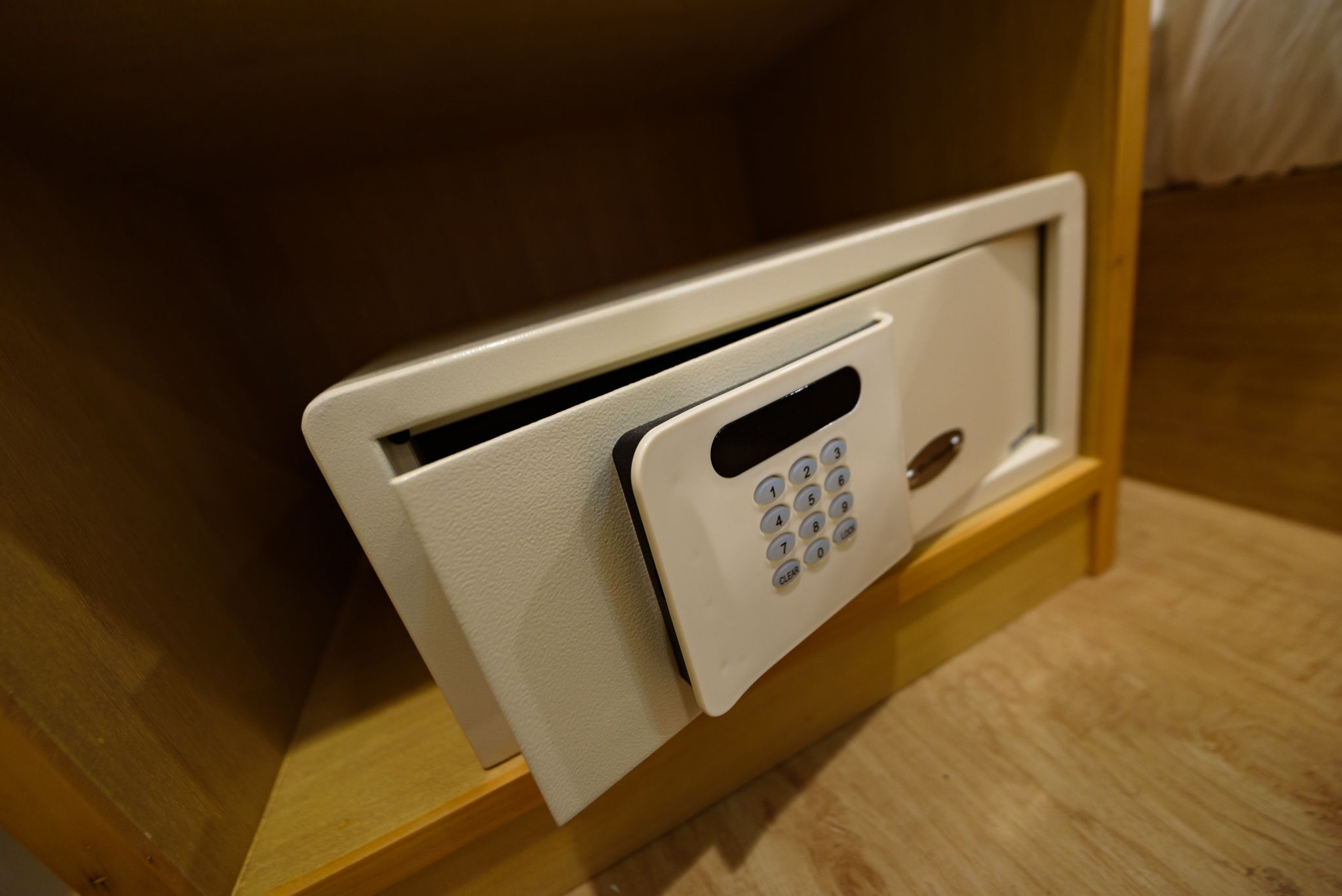 A white electronic keypad mounted on a wooden surface, likely part of a room's security system.