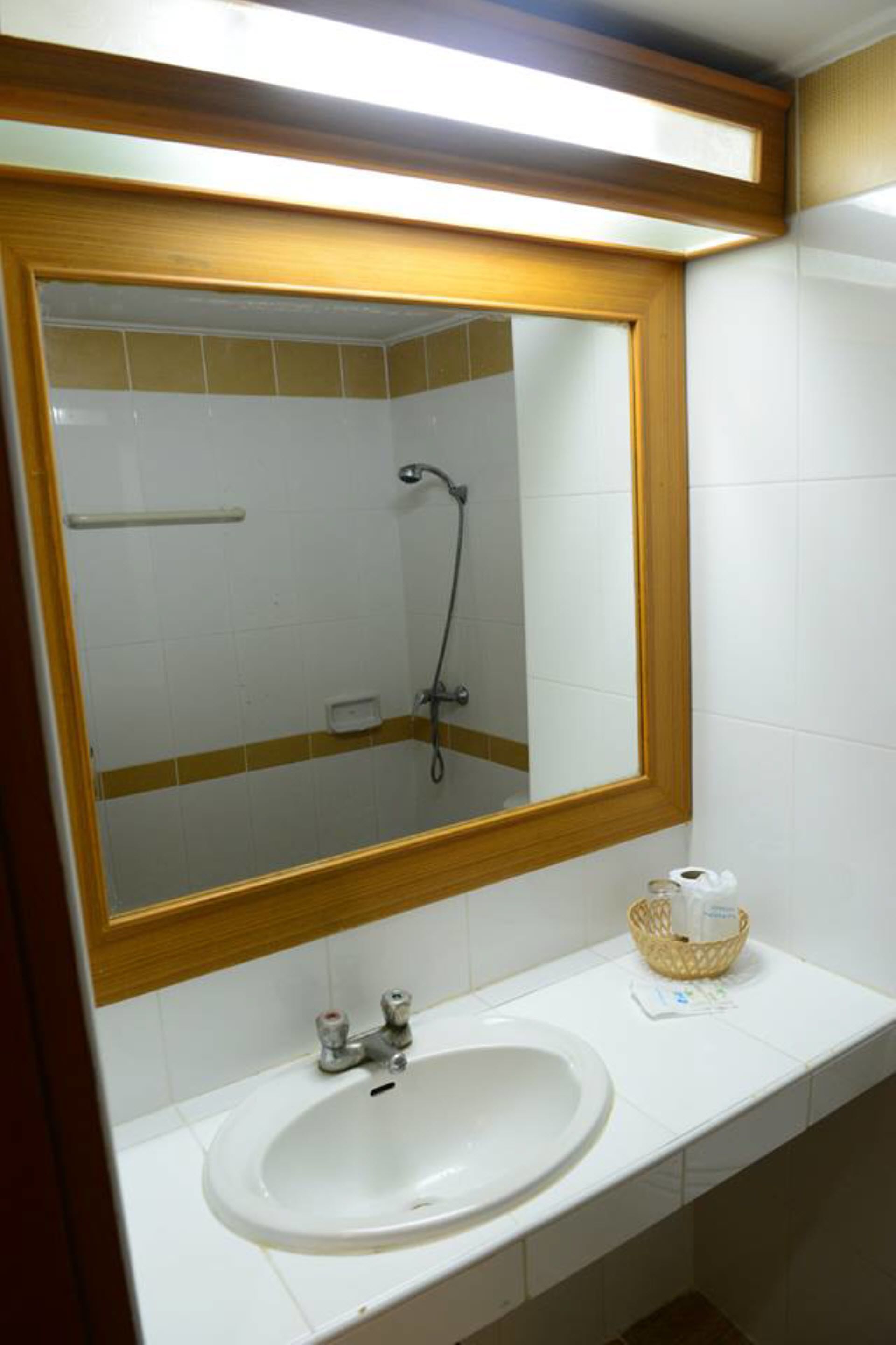 A bathroom with a wooden-framed mirror, a white sink, and a shower visible in the background.