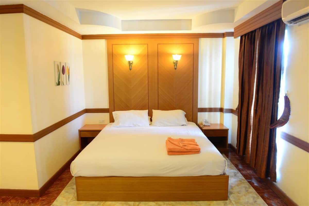 A hotel room with a large bed, two bedside tables, a nightstand, a wooden headboard, and a window with curtains.