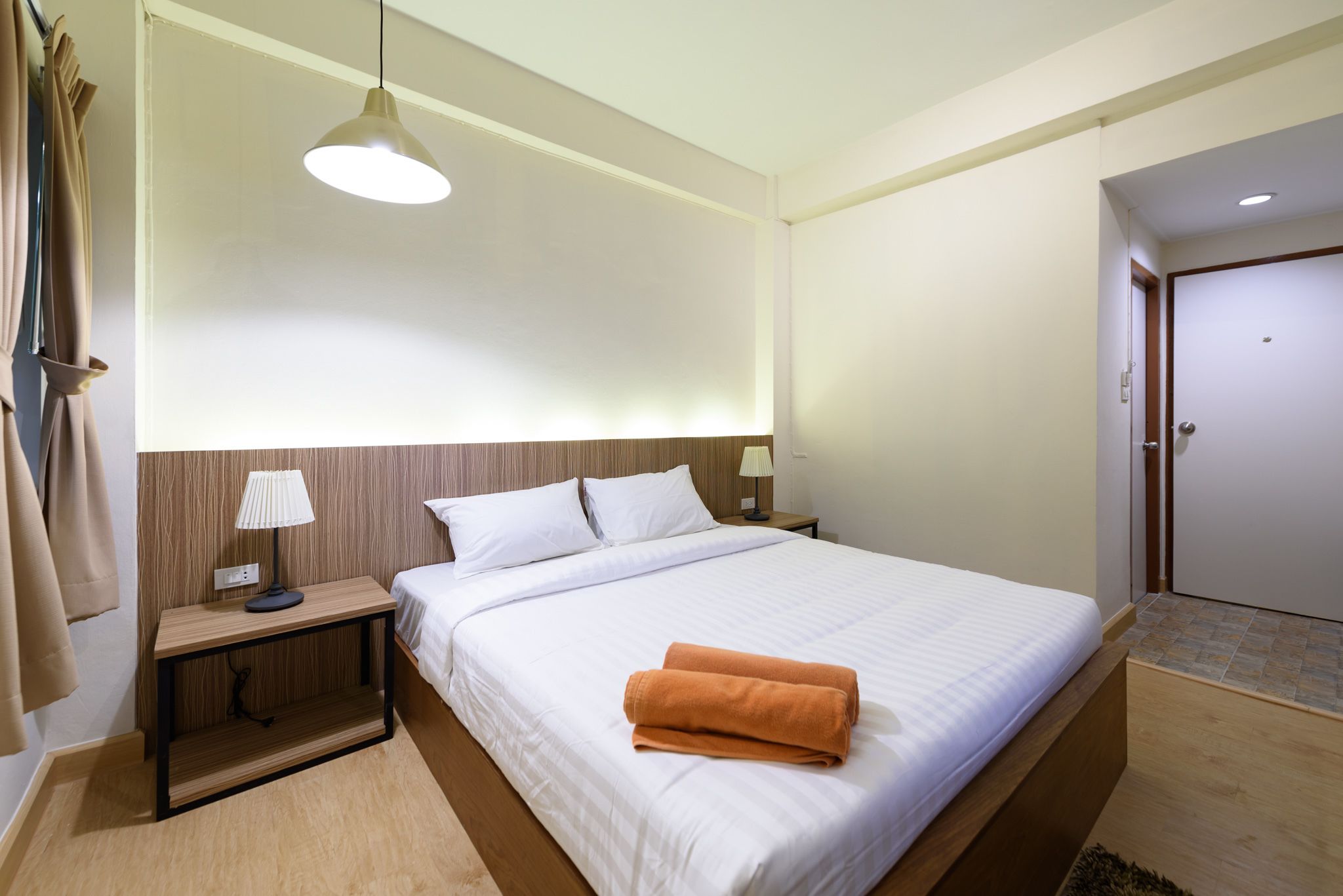 A hotel room with a large bed, a nightstand with a lamp, a wooden headboard, and a door.