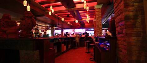 Un bar intérieur à l’éclairage rouge, avec des lanternes suspendues et des murs en briques.