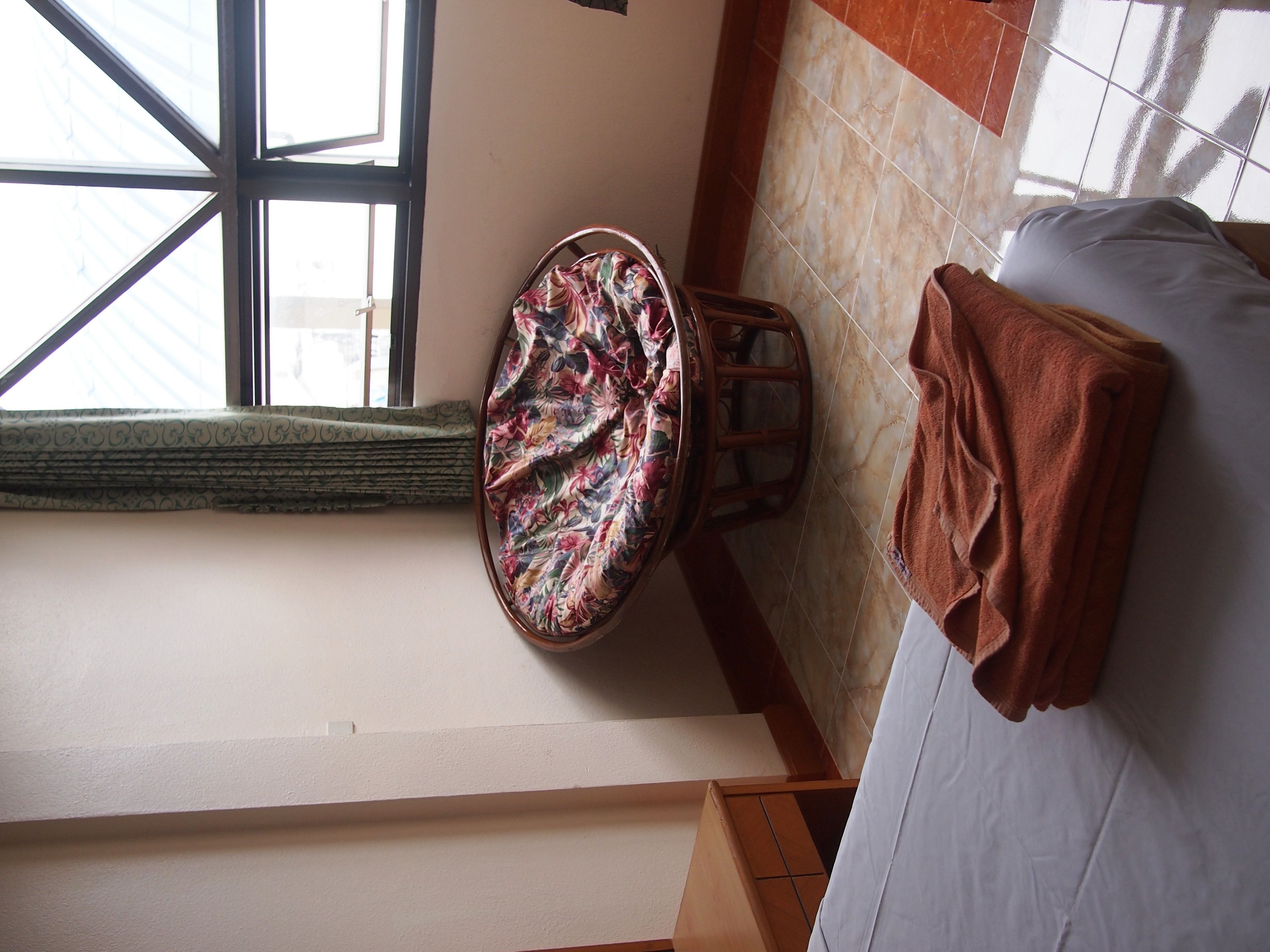 Une salle de bain avec des toilettes, un tabouret en bois, une serviette et une fenêtre donnant sur des immeubles.