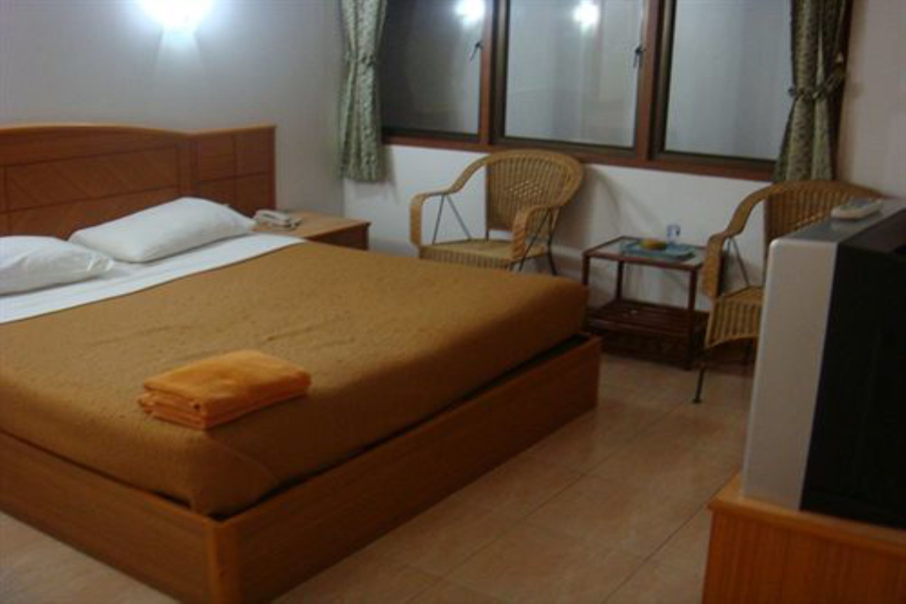 Quarto com uma cama grande, mesa de cabeceira, cadeira, mesinha e televisão.