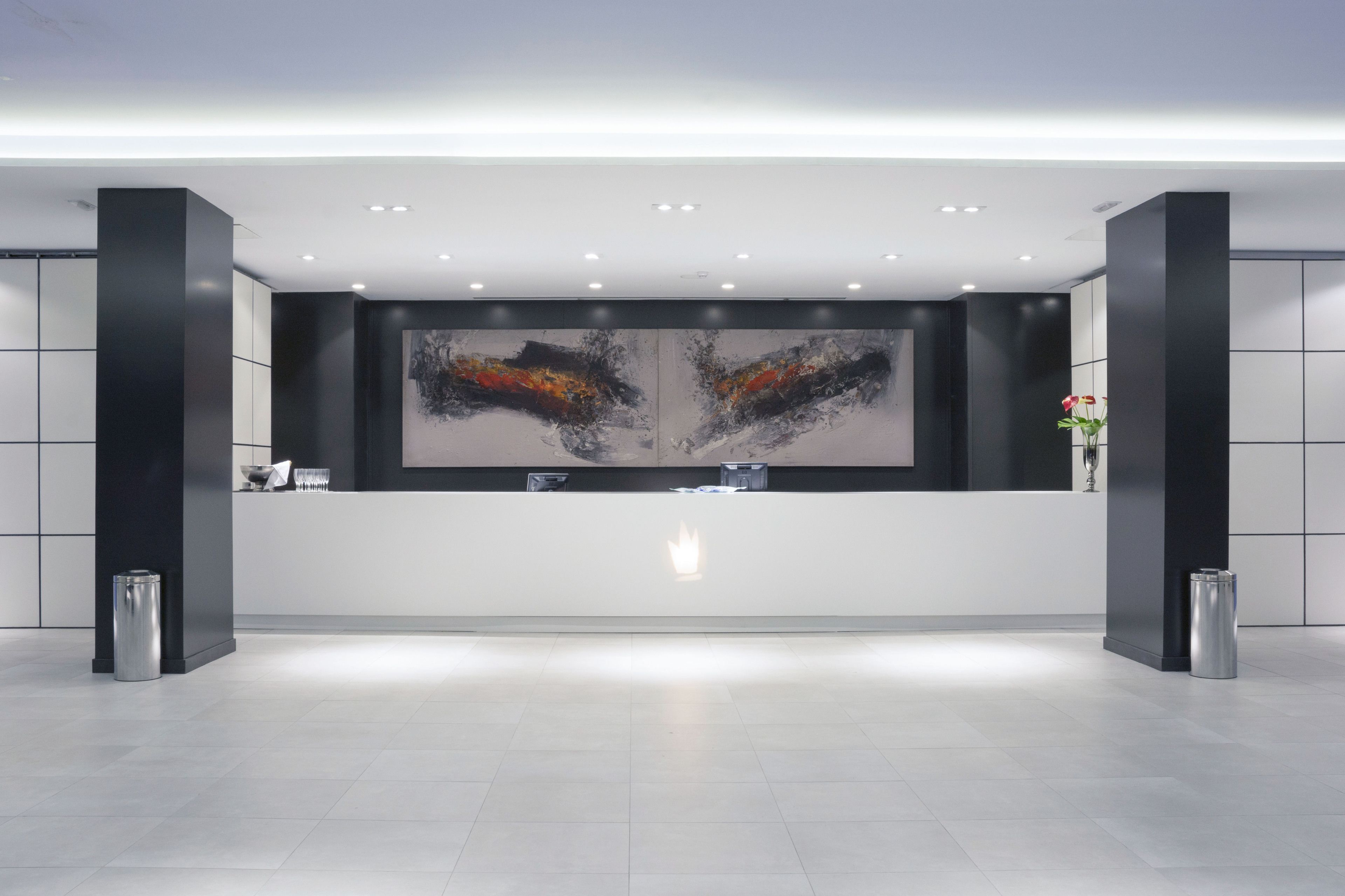 A modern reception area with a large abstract painting, a reception desk, and two trash bins.