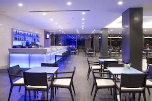 A modern restaurant with a long counter, multiple tables, and chairs.