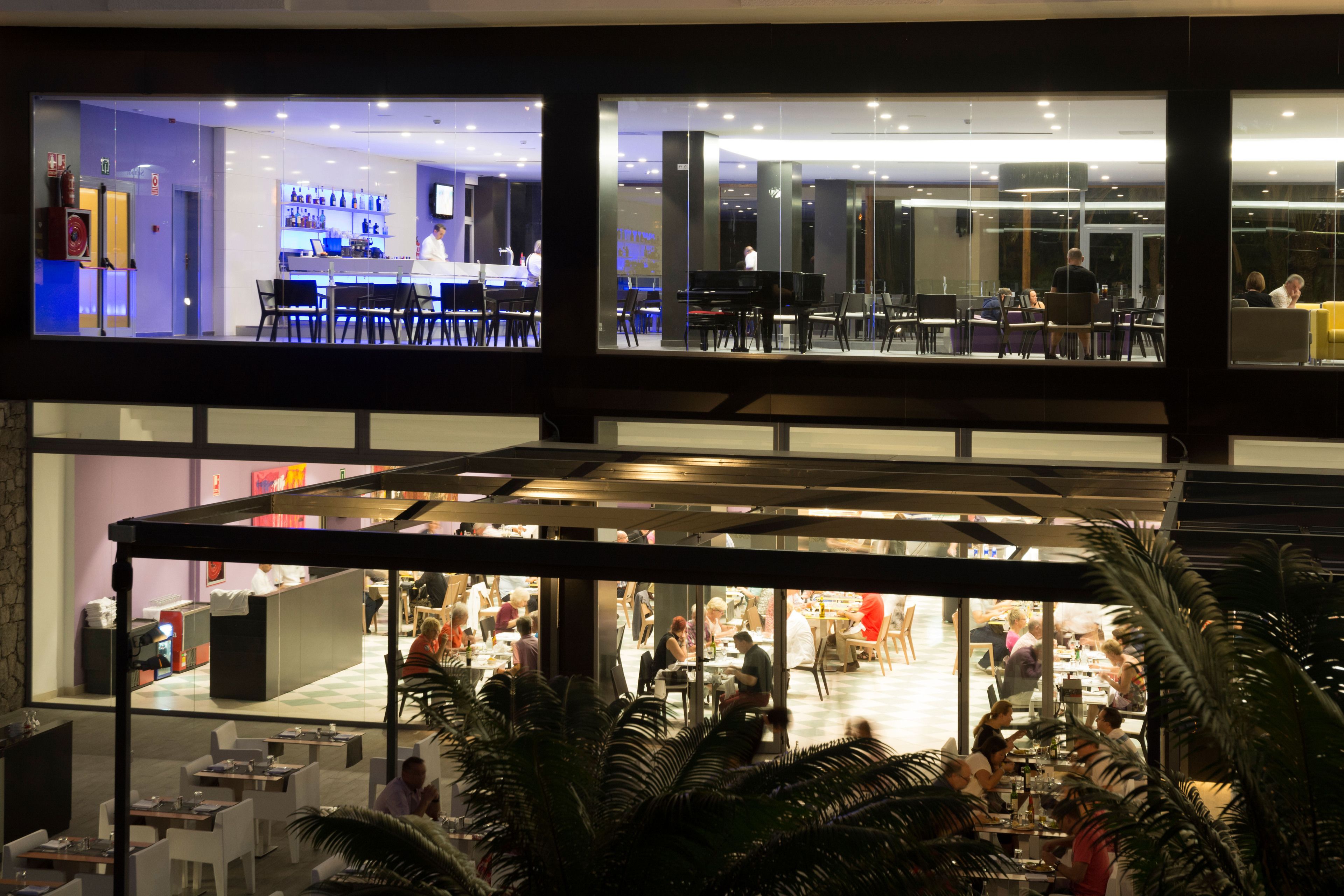A multi-level indoor space with dining areas, a piano, and a reception desk.