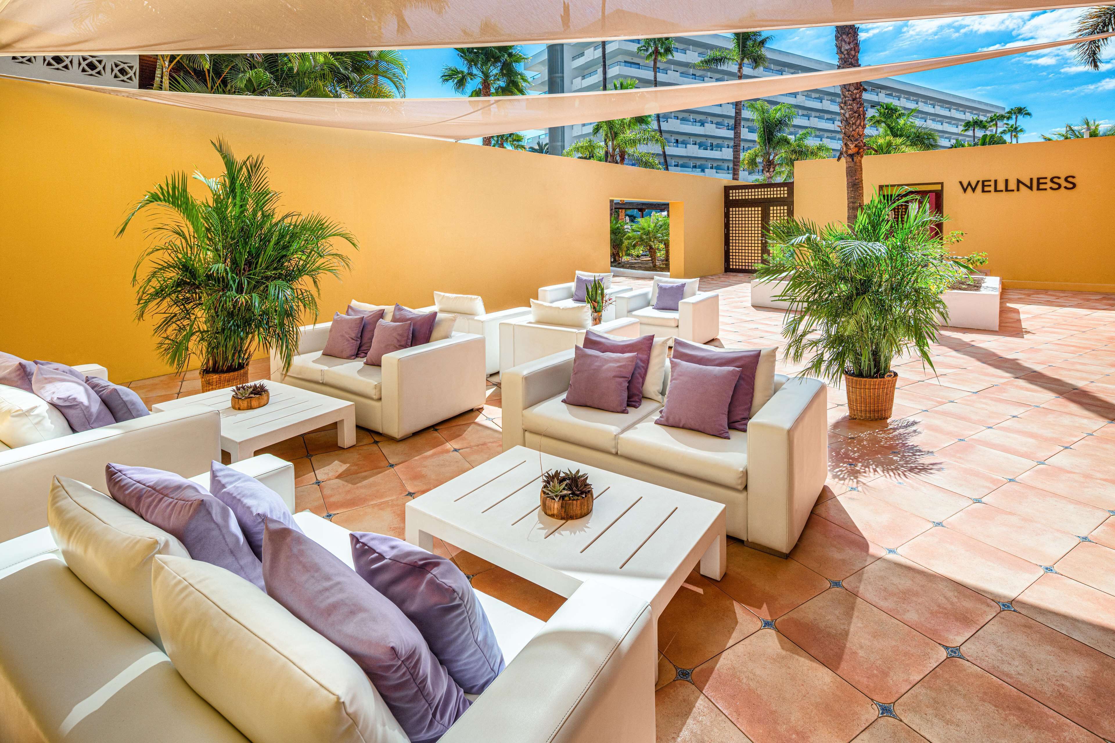 A wellness area with white sofas and purple cushions, surrounded by potted plants and a tiled floor.