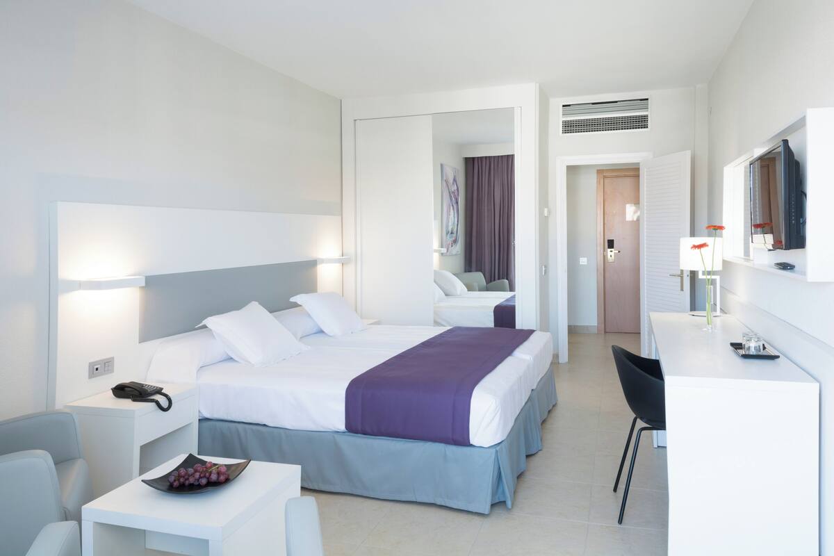 A modern hotel room with a large bed, a desk, a chair, and a bathroom visible through an open door.