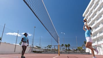 Una cancha de tenis con una red, dos jugadores y un edificio al fondo.