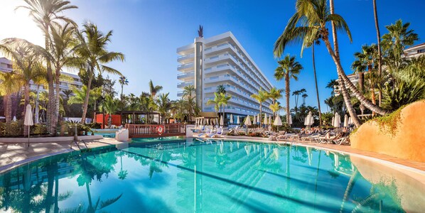 A hotel pool area with a clear blue pool, palm trees, and a multi-story building in the background. - Hotel Gran Canaria Princess - Adults Only (+16) (San Bartolomé de Tirajana)