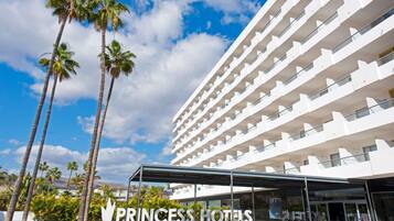 Un hotel de varios pisos con diseño moderno, que cuenta con un acceso cubierto y palmeras en primer plano.