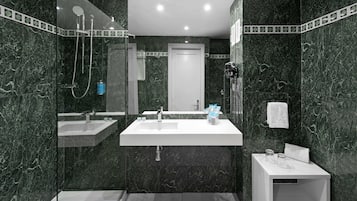 A modern bathroom with a large mirror, two sinks, a shower, and a small bedside table with a towel.
