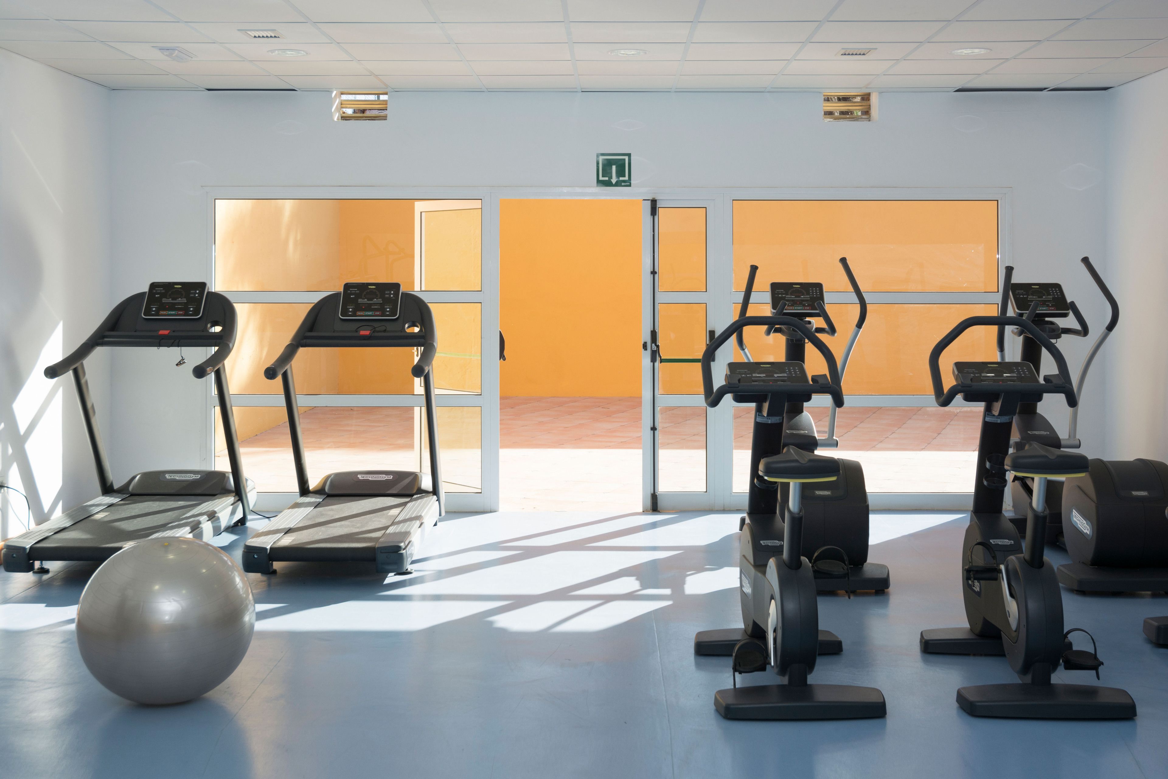 Un gimnasio con cintas de correr, elípticas y una pelota de ejercicios grande.