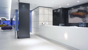 A modern reception area with a white reception desk, a large abstract painting on the wall, and a seating area with yellow chairs. - Hotel Gran Canaria Princess - Adults Only (+16) (San Bartolomé de Tirajana)