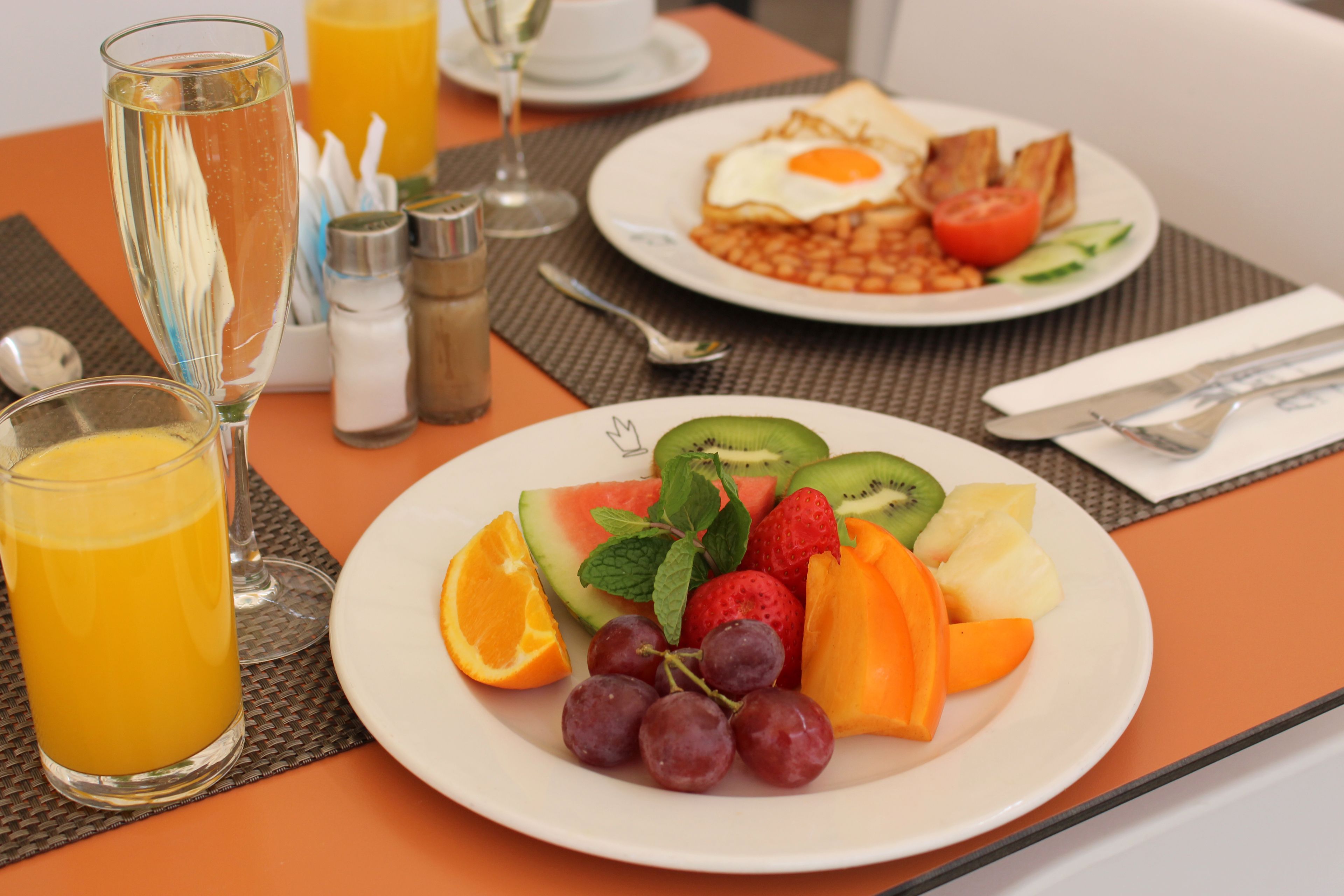 A breakfast setting with a plate of fruit, a glass of orange juice, and a glass of white wine.