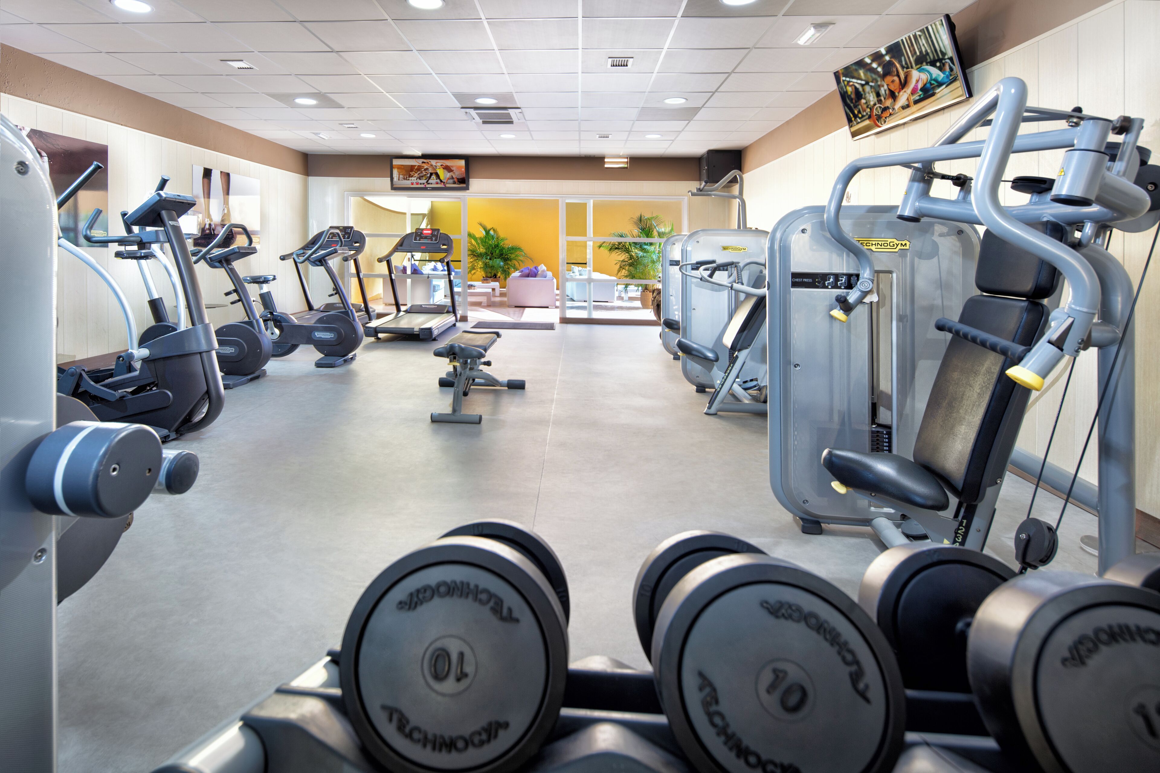 Een sportschool met diverse fitnessapparaten, waaronder loopbanden, elliptische trainers en krachttrainingsmachines.