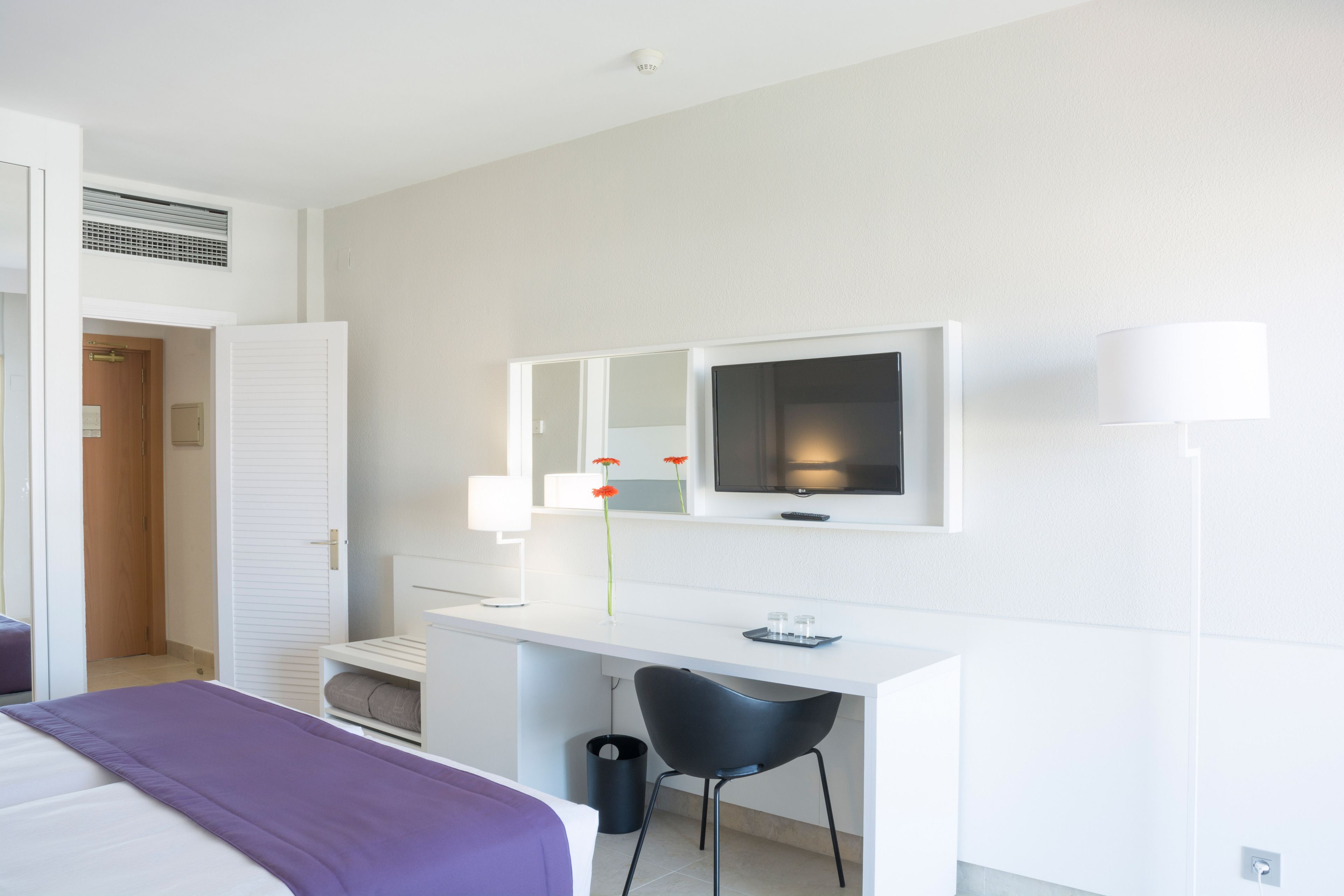 Una habitación de hotel con una cama, un escritorio con una silla, un televisor y un espejo.