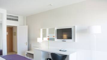 Una habitación de hotel con una cama, un escritorio con una silla, un televisor y un espejo.